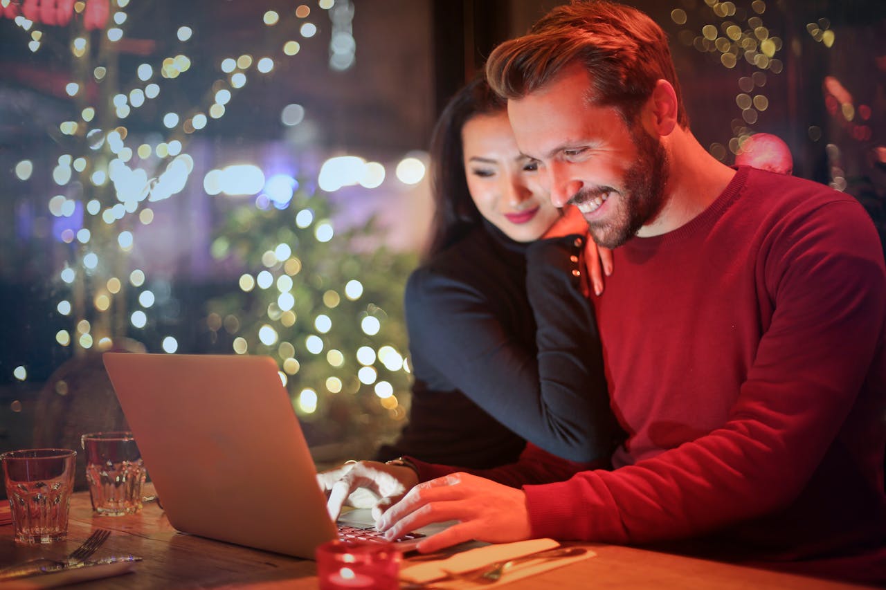 Crafting Captivating Headlines: Your awesome post title goes here A couple using a laptop at a cozy restaurant with festive bokeh lights, enjoying online shopping together.